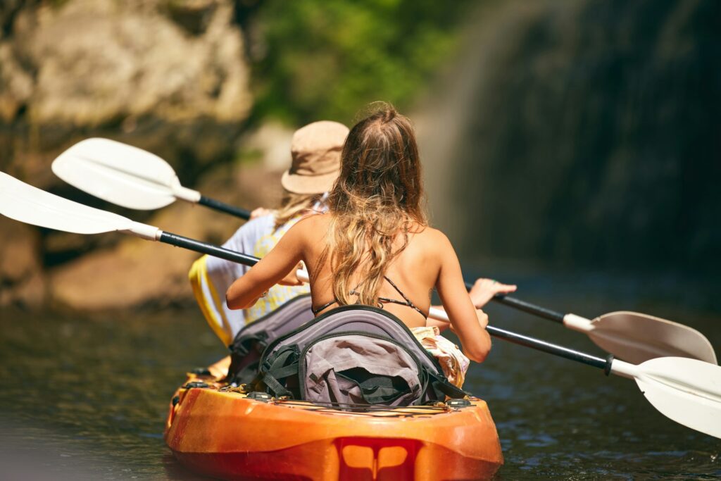 Women friends rowing a kayak or boat on a river or lake while on summer vacation or travel. Tourist